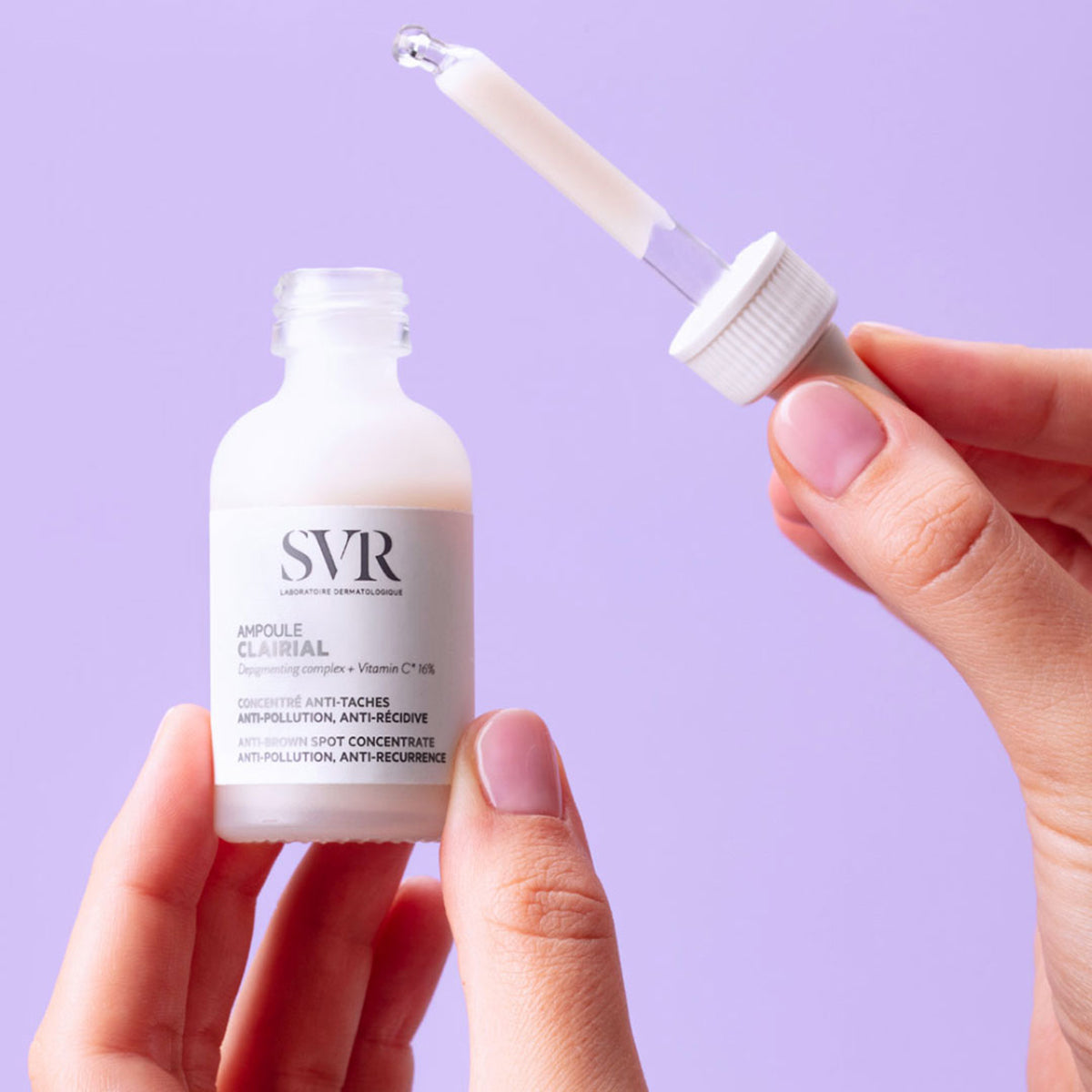 Manos de una mujer sosteniendo el Ampoule de Clairial de SVR y en la otra mano el gotero de aplicación en un fondo morado