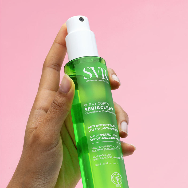 Una mano sosteniendo el envase del Spray Corps de Sebiaclear con un fondo en rosa