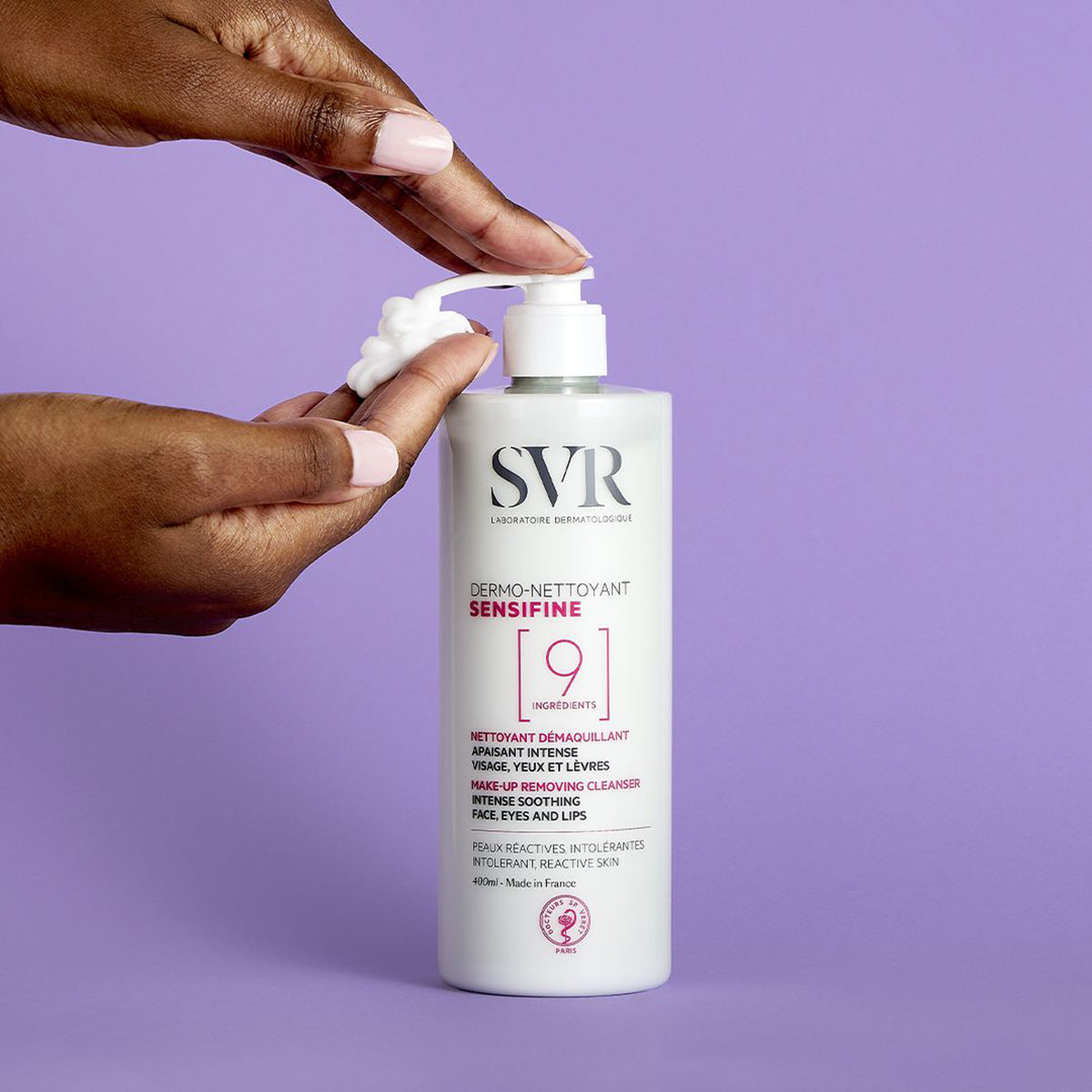 Dos manos de tez morena, mostrando en una mano aplicandose del dispensador del producto SENSIFINE Dermo-Nettoyant en un fondo morado