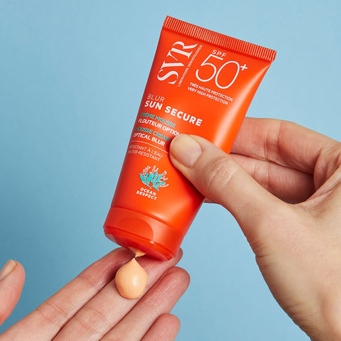 Manos de una mujer de tez clara aplicando en una de sus manos el Sunsecure Blur 50+SPF de SVR en un fondo azul