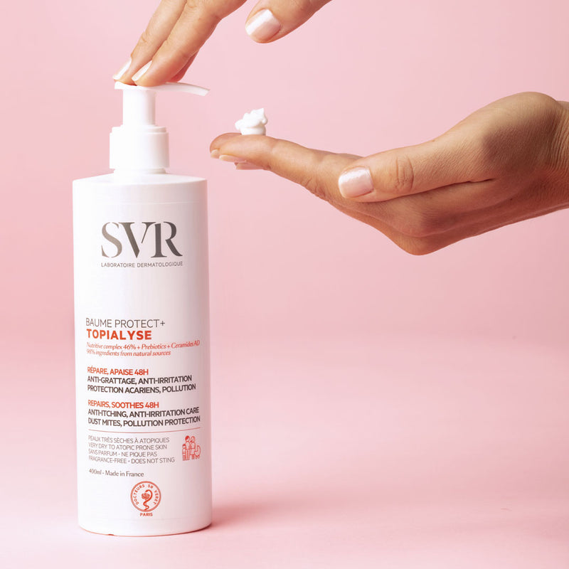 Una mujer aplicandose en la mano con el dispensador el Baume protect+ TOPIALYSE, en fondo rosa, para pieles secas y sensibles.