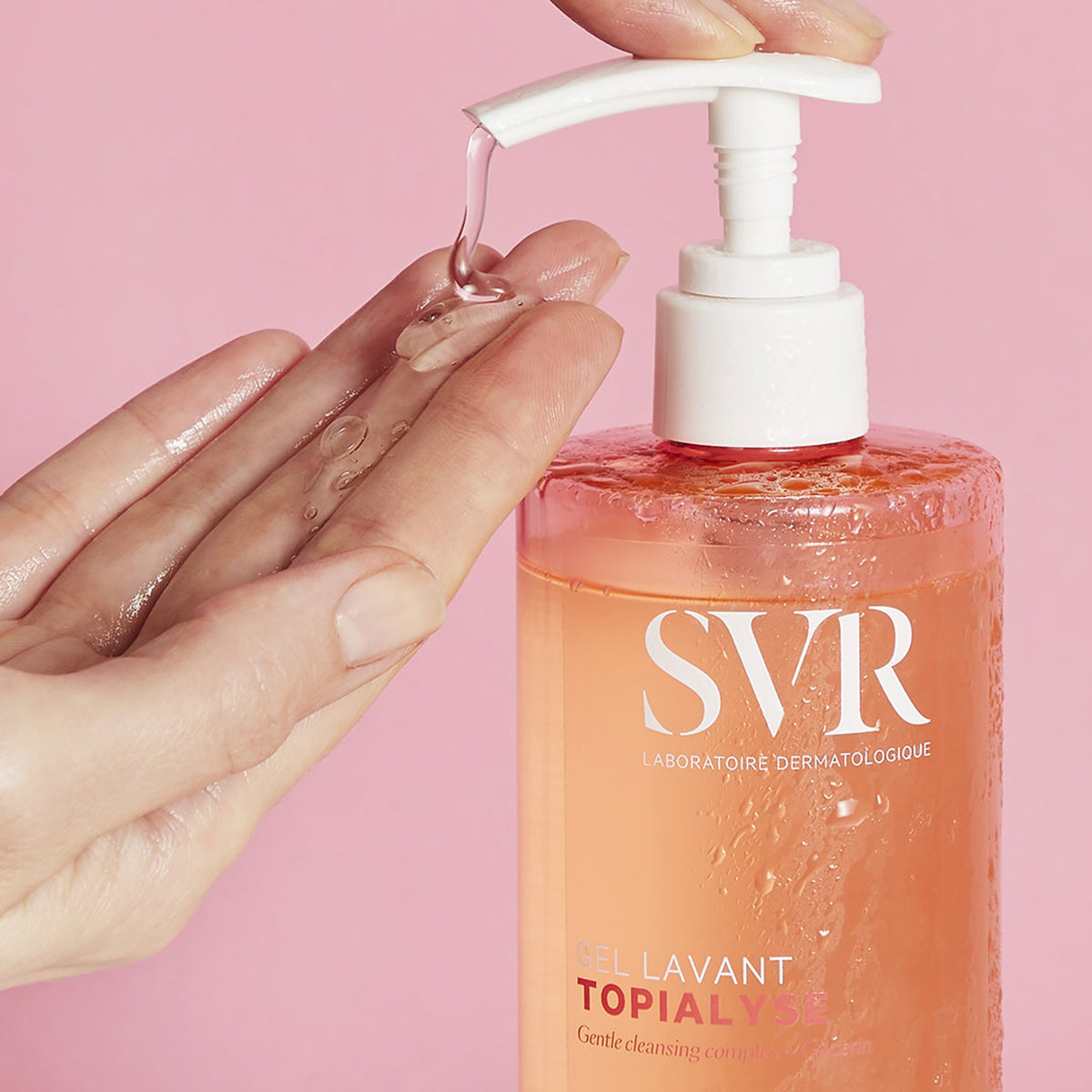 Manos de mujer aplicandose en una de sus manos el producto Topialyse el lavant en un fondo rosa