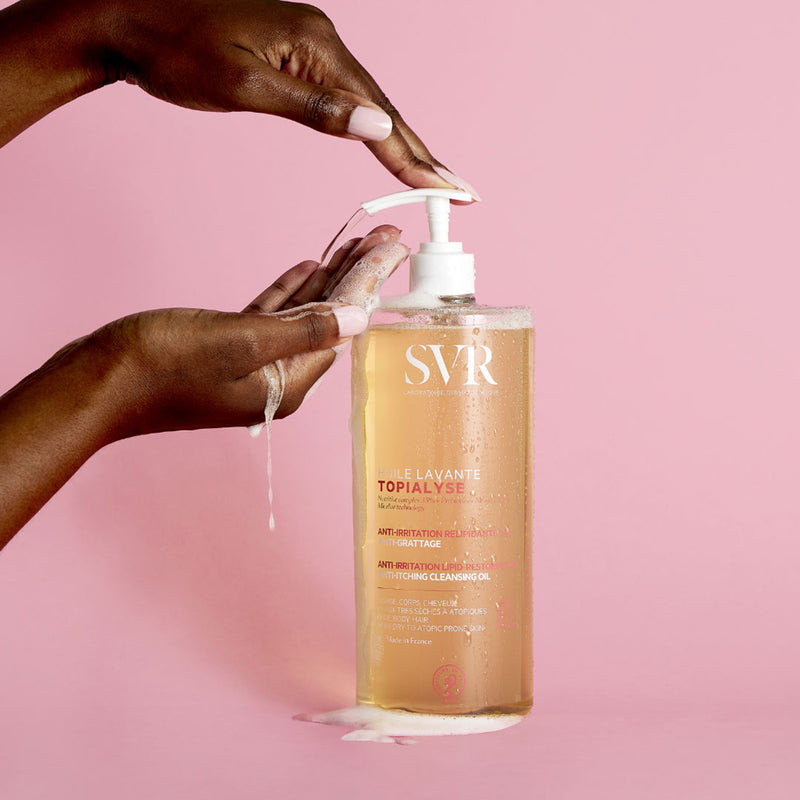 Manos de una mujer de tez morena aplicando en una de sus manos el producto de forma liquida transparente de ligera espuma con fondo rosa