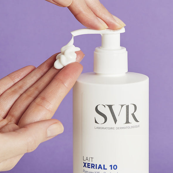 Un par de manos aplicando producto en una de sus manos de forma cremosa del dispensador del Xerial 10 Lait de SVR, con fondomorado