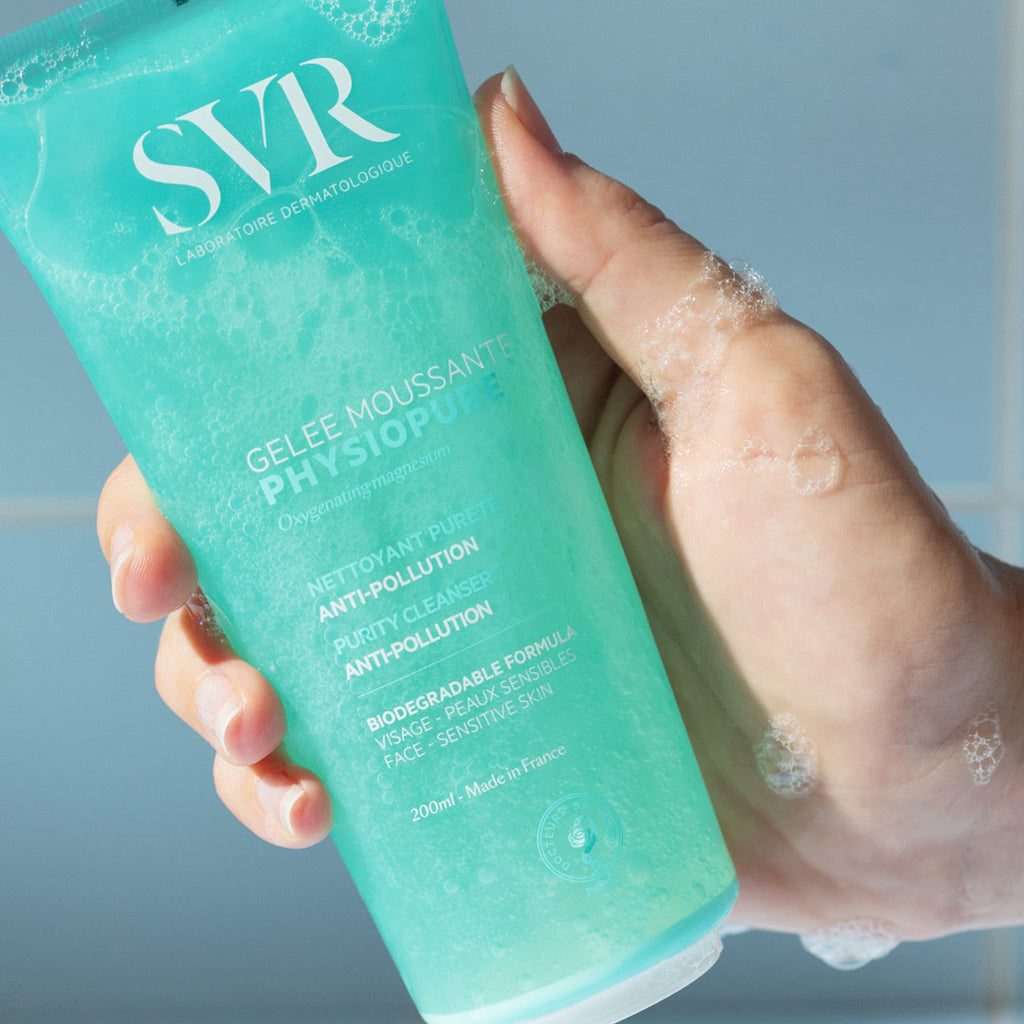 Una mano de tez clara mostrando el producto del gel PHYSIOPURE Gelee Moussante con espuma en la mano en un fondo azul