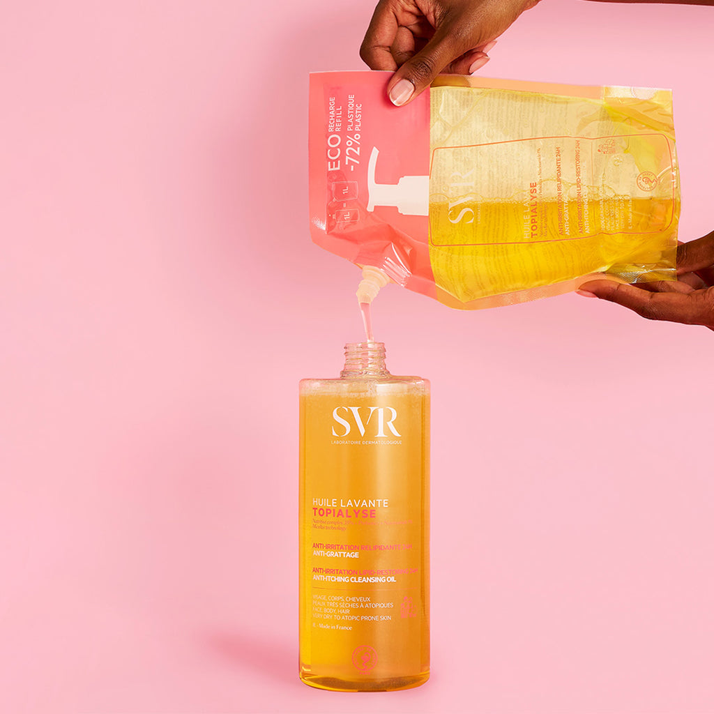 manos de mujer rellenando una botella de Huile Lavante de SVR de un eco refil en un fondo rosa