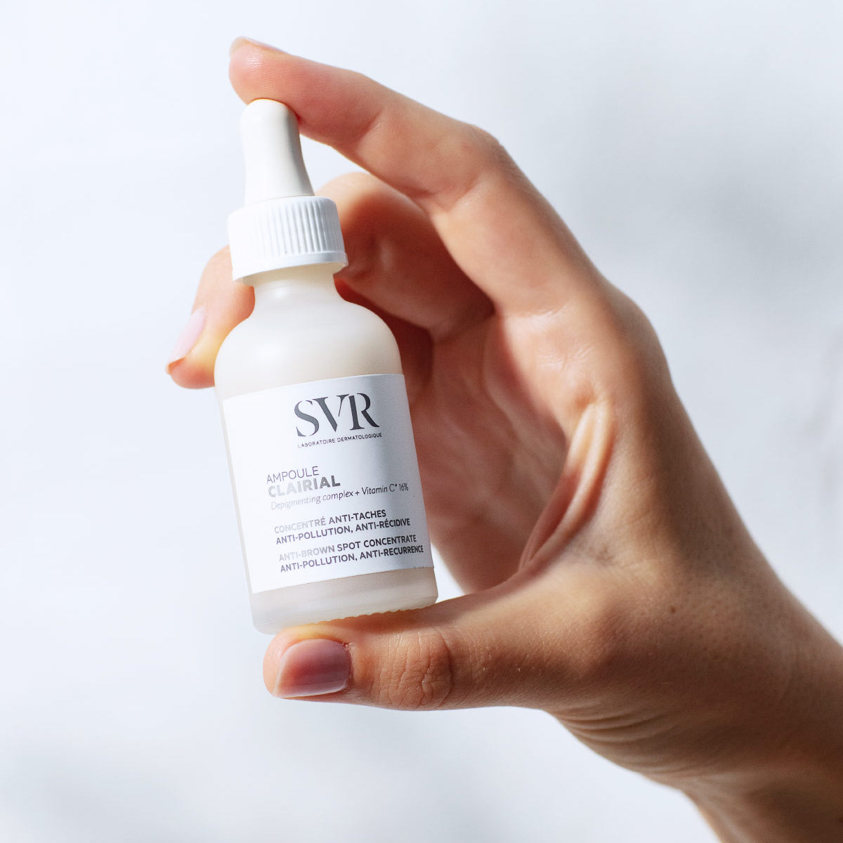 Mano de una mujer sosteniendo el envase del Ampoule Clairial de SVR en un fondo claro