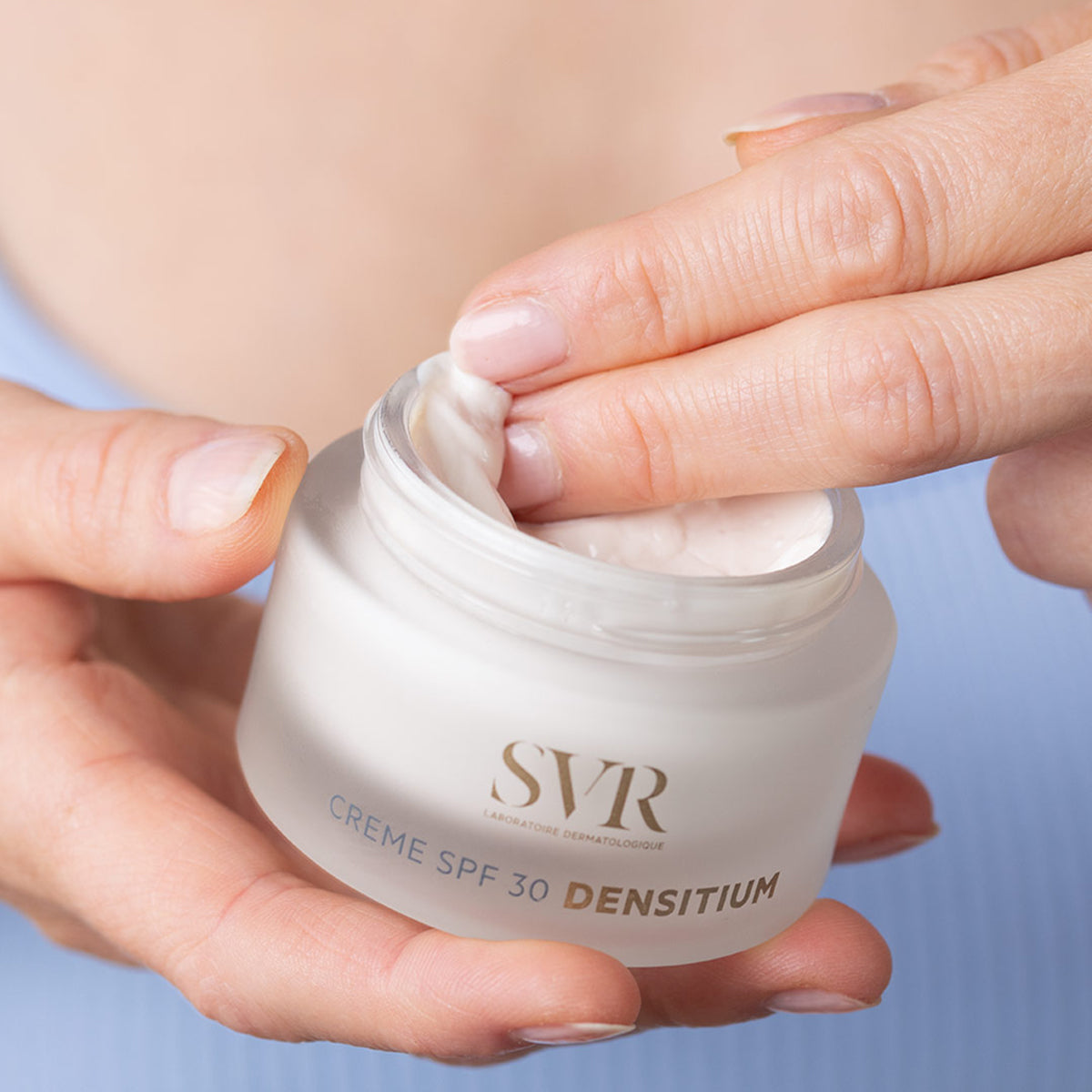 Manos de una mujer sonteniendo con una mano, y con la otra tomando producto de la Creme SPF 30 Densitium de SVR