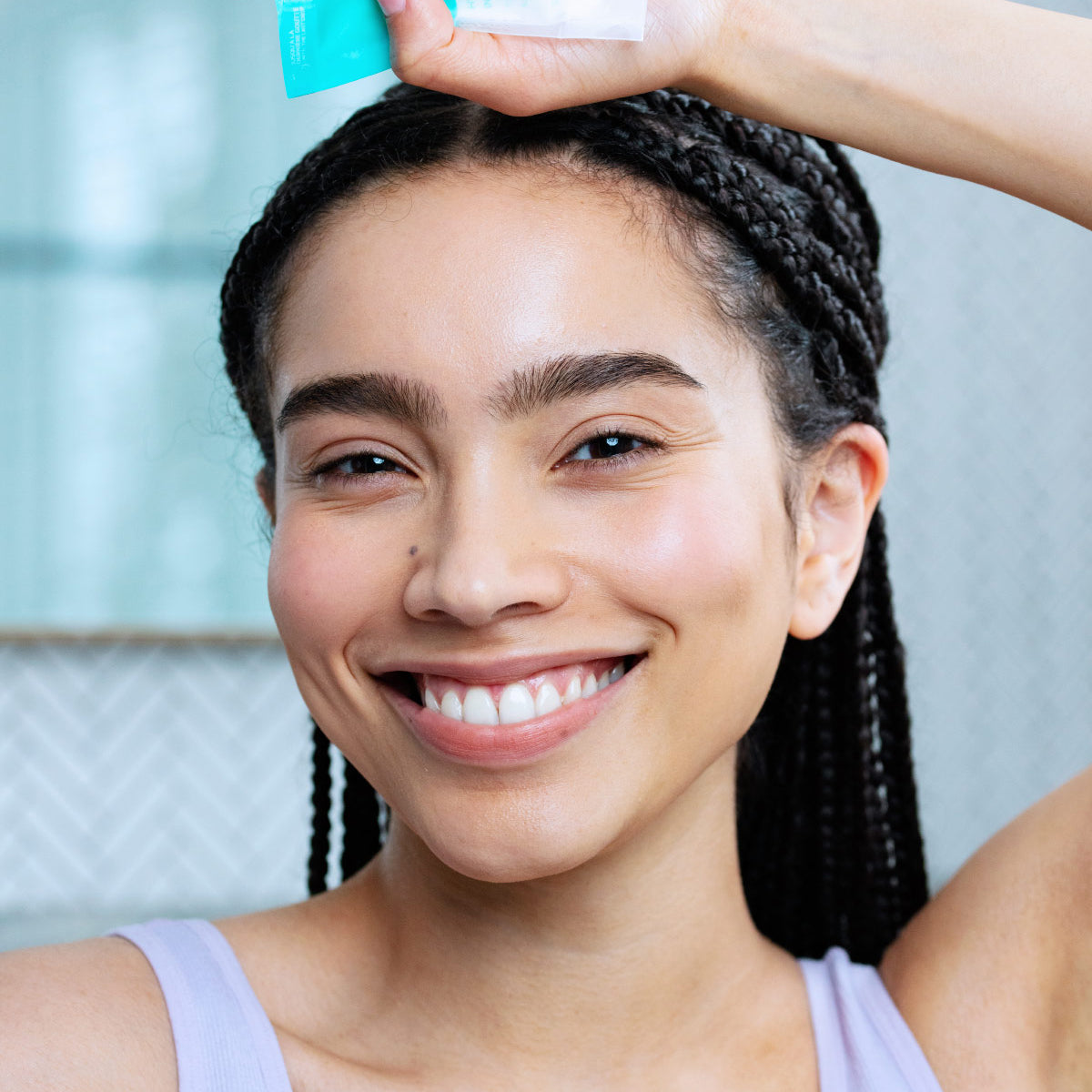 Mujer de tez morena clara sonriendo con trenzas, sosteniendo en una de sus manos sobre su cabeza la creme Hydraliane de SVR