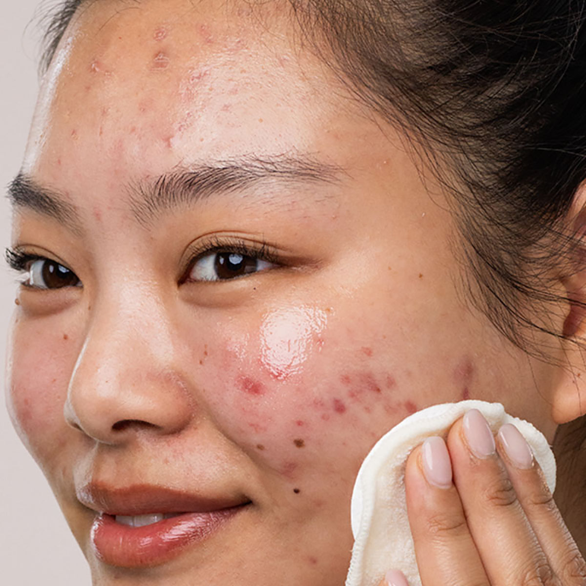 Mujer asiatica de cabello obscuro limpiando con un algodon su rostro con el SEBIACLEAR EAU Micellaire con fondo claro