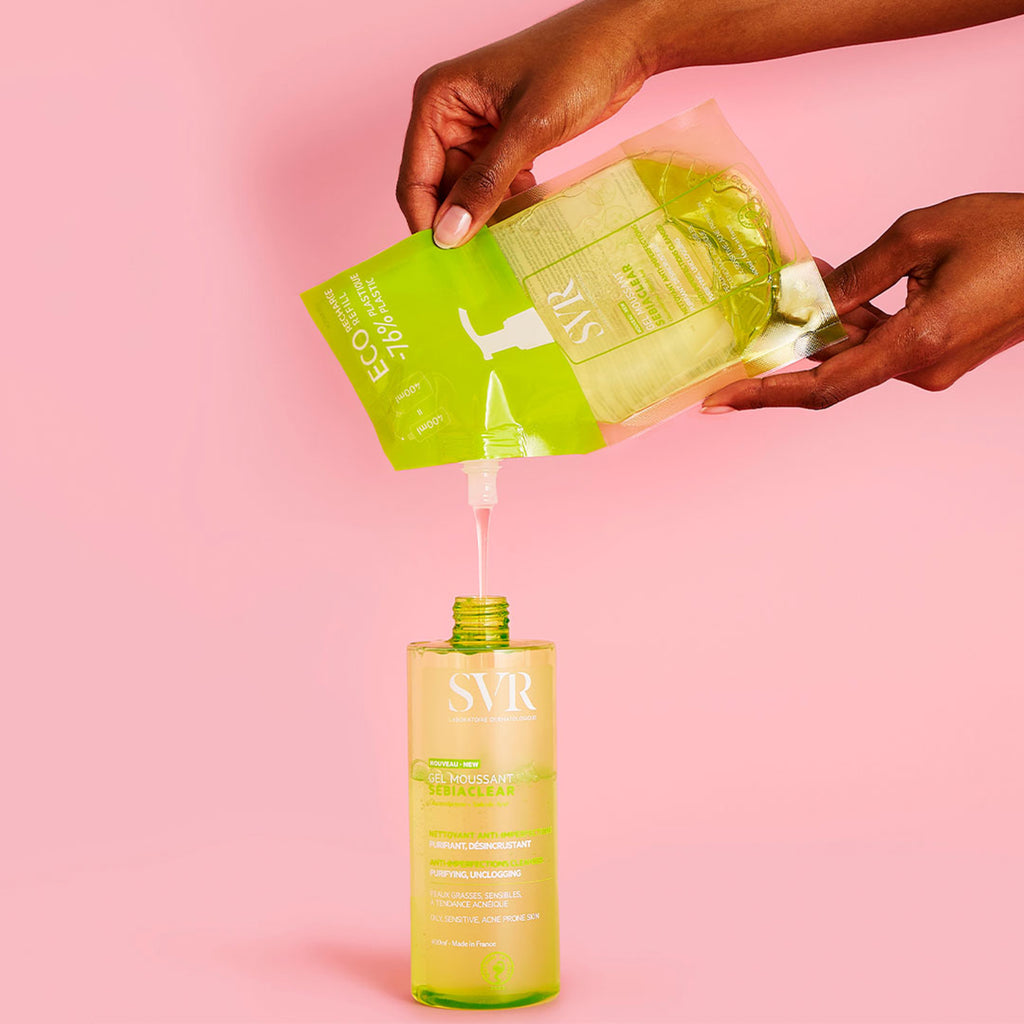 Manos de una mujer rellenando una botella del eco refill a una botella de 400 ml del SEBIACLEAR Gel Moussant para pieles con tendencia acneica, en un fondo rosa