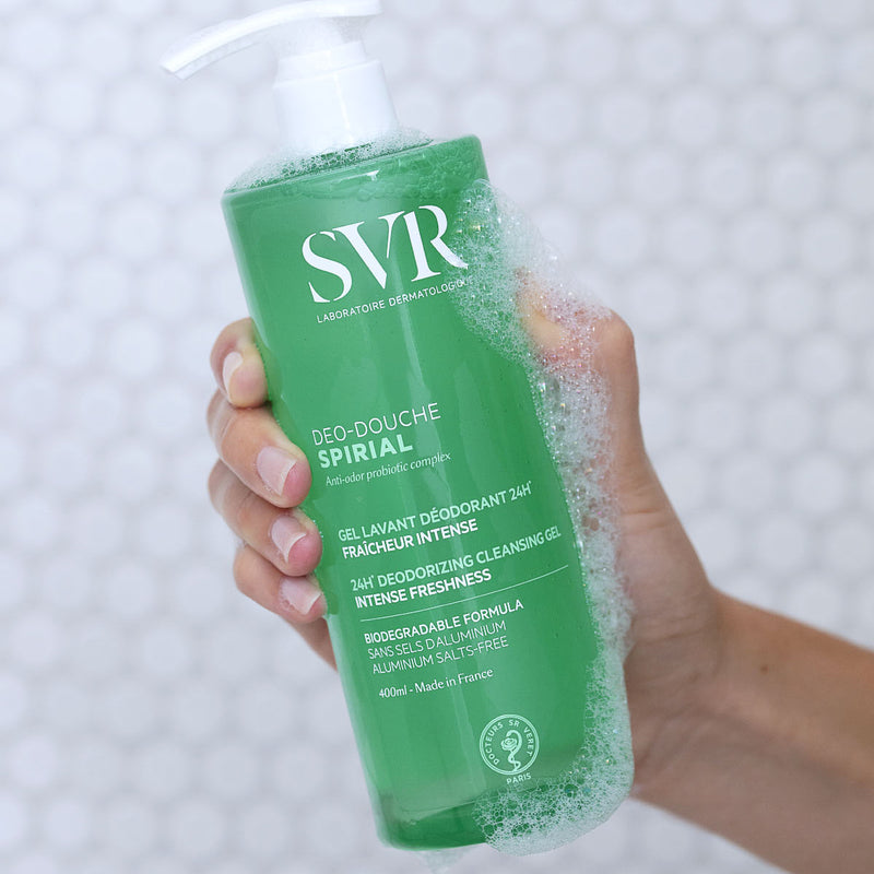 Una mano de tez clara , mostrando una botella de 400 ml del producto con jabon y espuma en la mano del Deo-Douche SPIRIAL gel limpiador y desodorante con fondo blanco