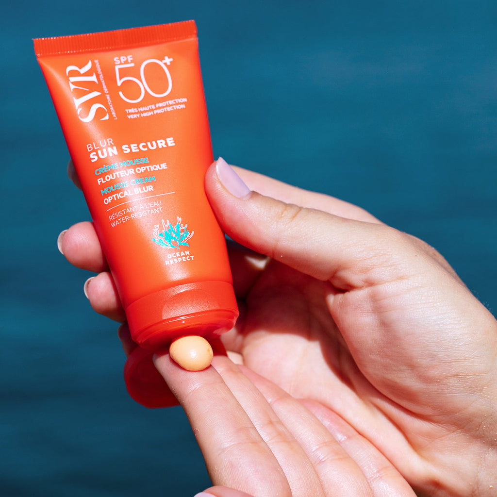 Manos de una mujer aplicando producto en una de sus manos del Protector solar Blur Sunsecure SPF+50 de SVR de fondo el mar