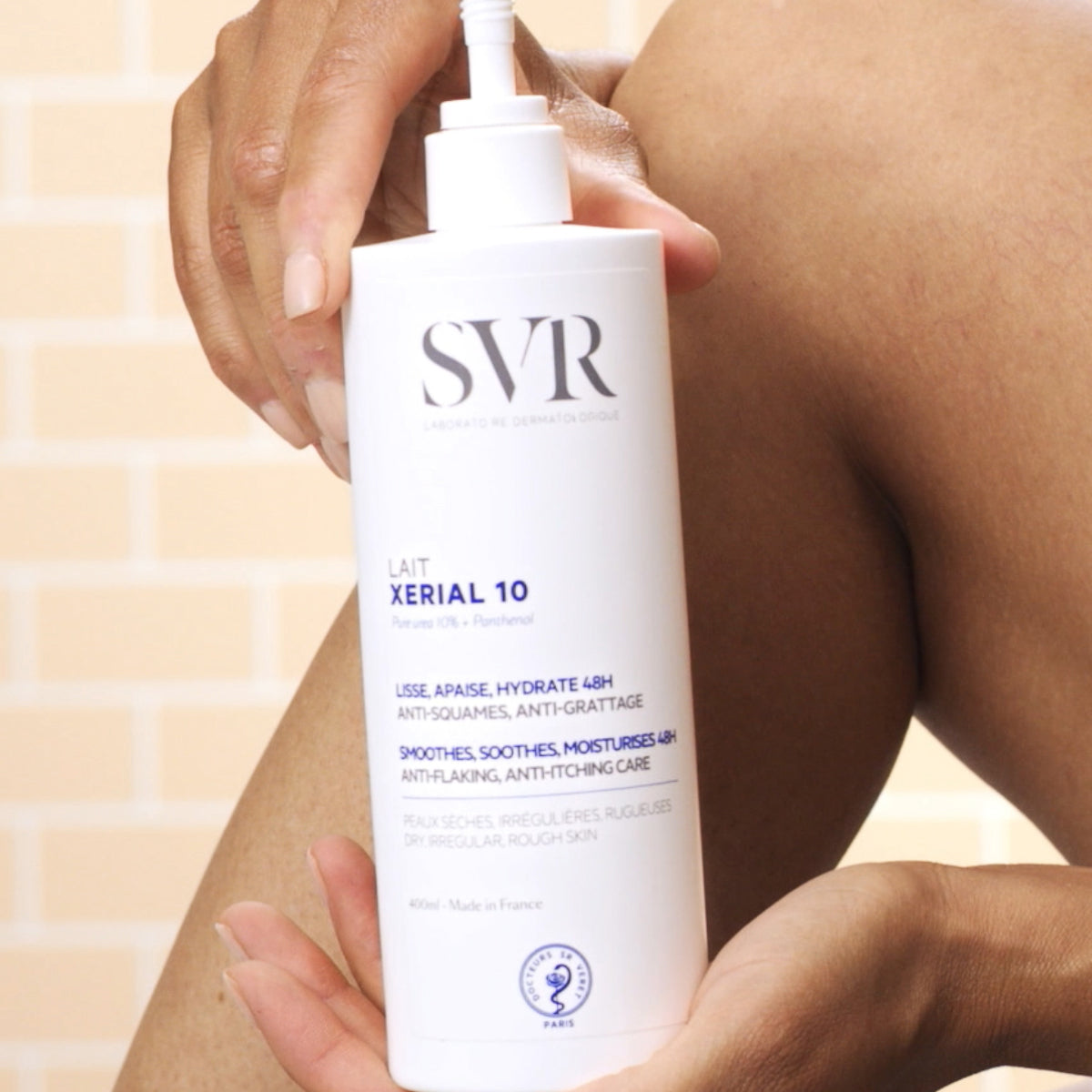 Una mujer mostrando el producto tomando entre sus manos del Lait XERIAL 10 de SVR y se muestra una parte de la pierna con un fondo de ladrillo claro
