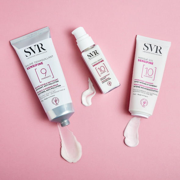 Productos de la gama Sensifine de SVR, Baume demaquillant, Hydra-creme, Masque SOS mostrando producto de las texturas de cada envase en un fondo rosa