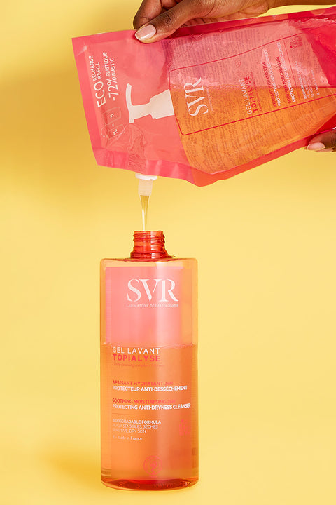 Unas manos de mujer rellenado una botella de Topialyse Gel Lavat de un empaque de refil en un fondo rosa