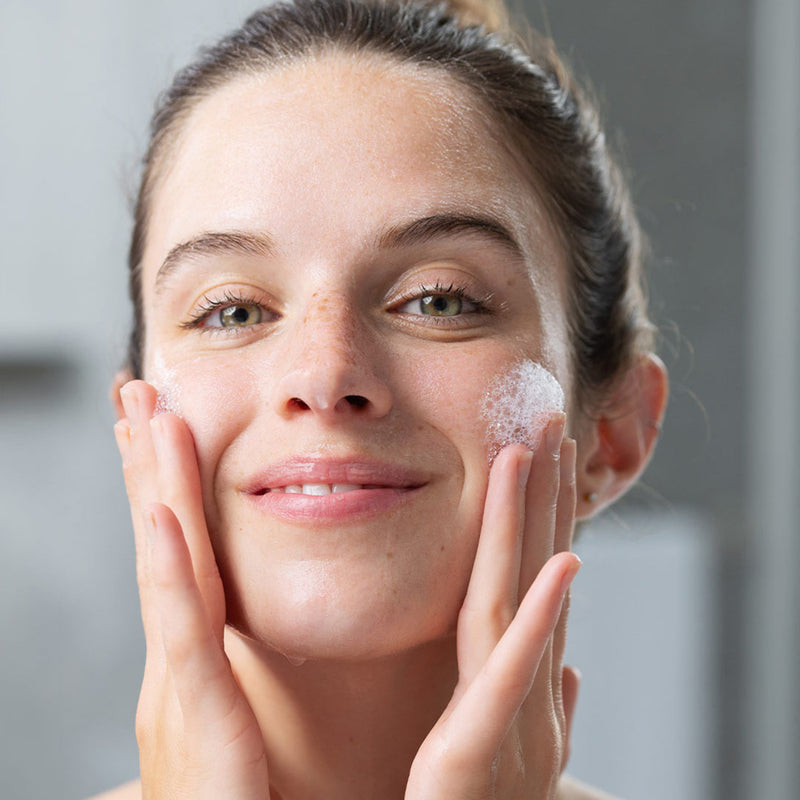 Rostro de mujer de tez clara con pecas en la nariz aplicando producto en una de sus mejillas generando espuma del producto PHYSIOPURE Gelee Moussante de SVR