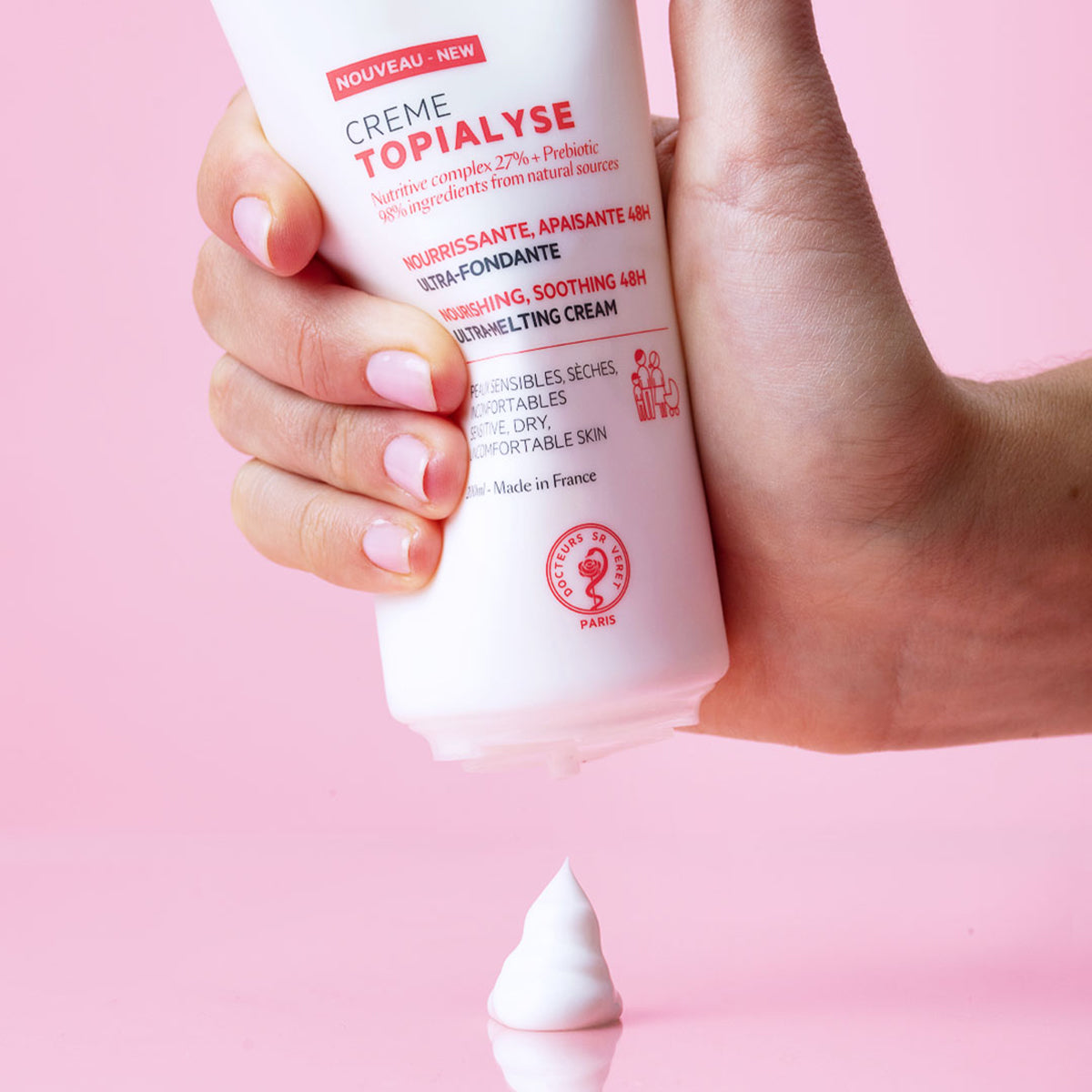 Producto envase de 200 ml de TOPIALYSE Crème en una mano de piel clara con fondo rosa