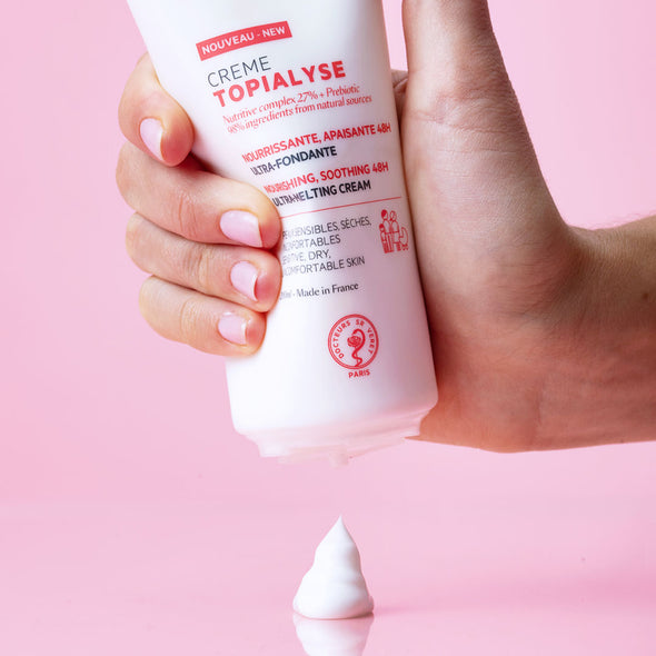 Producto envase de 200 ml de TOPIALYSE Crème en una mano de piel clara con fondo rosa