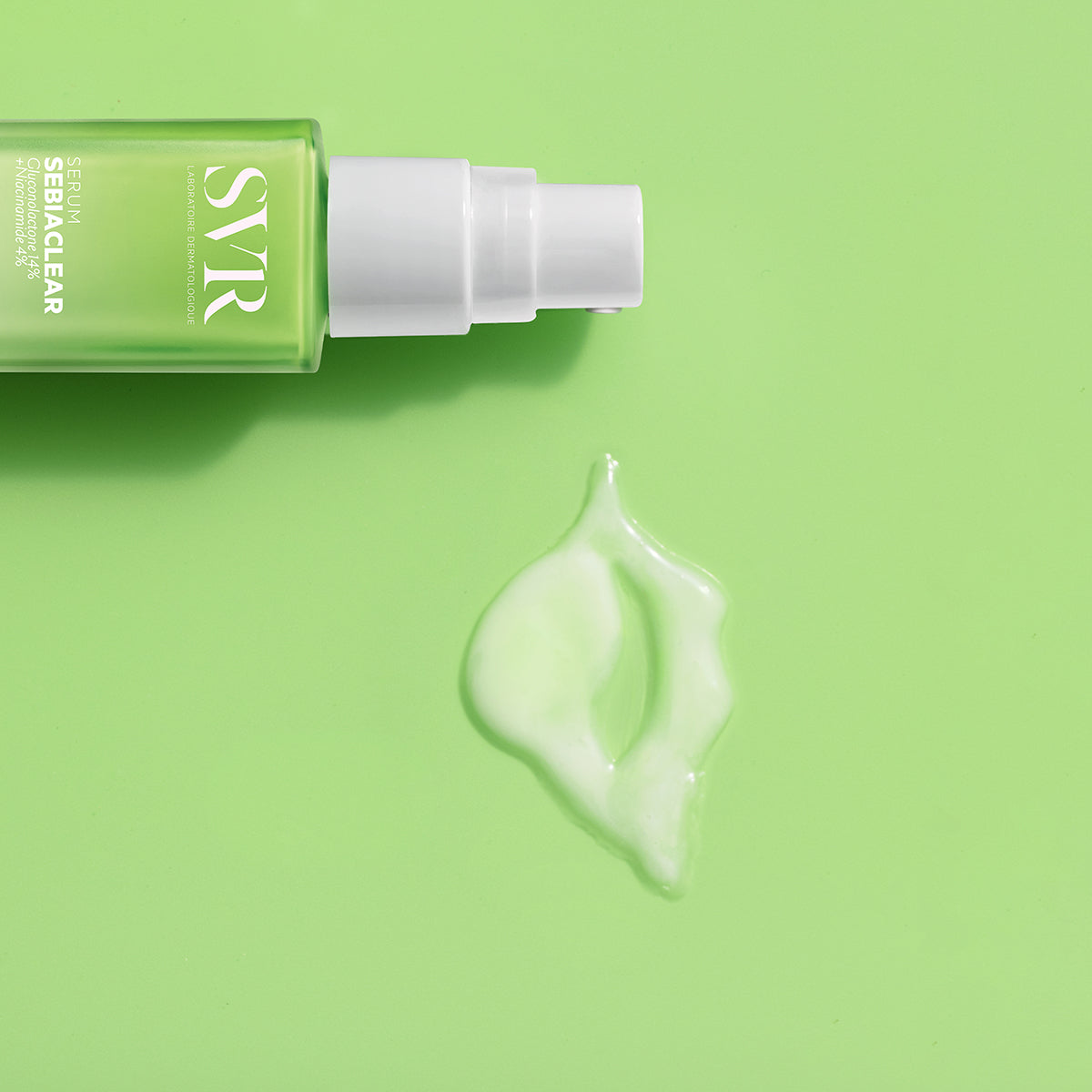 Frasco de suero SVR Sebiaclear verde con dosificador blanco y una gota de producto sobre fondo verde claro.