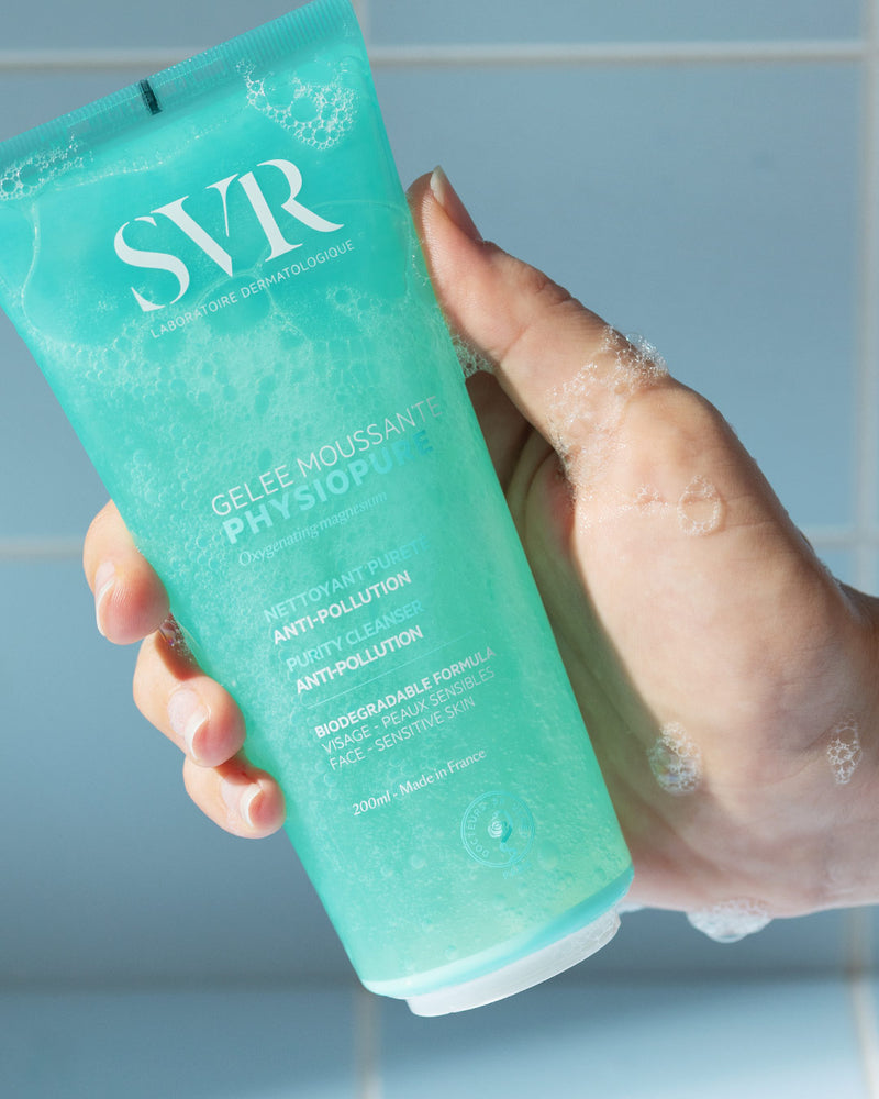 Una mano de tez clara mostrando el producto del gel PHYSIOPURE Gelee Moussante con espuma en la mano en un fondo azul